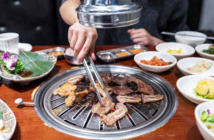 a person using tongs to turn meat cooking on a sunken bbq in a table