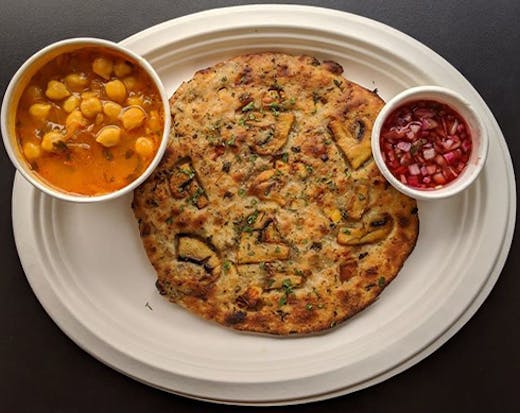 An Indian flat bread on a plate with a small bowl of curry