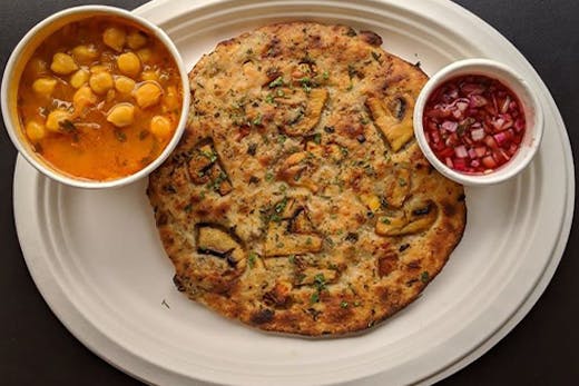 An Indian flat bread on a plate with a small bowl of curry