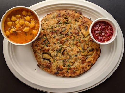 An Indian flat bread on a plate with a small bowl of curry