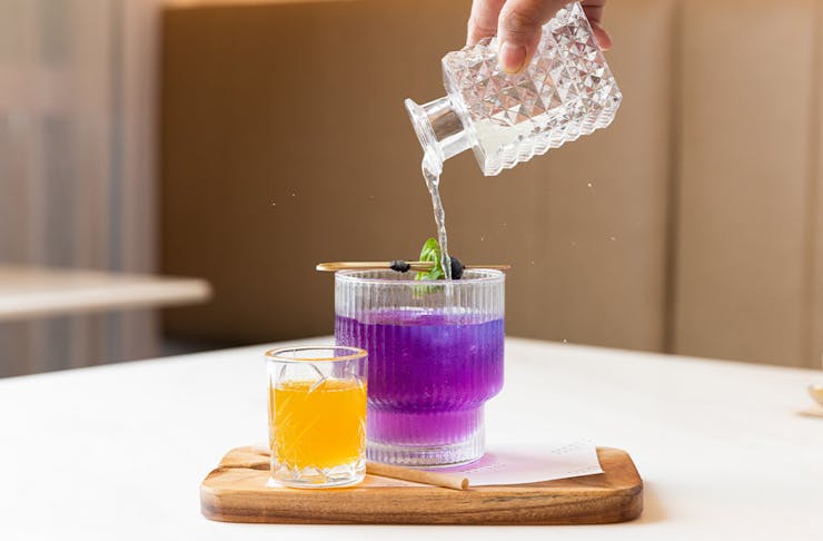 a hand pouring a purple drink into a glass