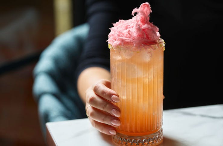A large peach-coloured cocktail topped with fairy floss