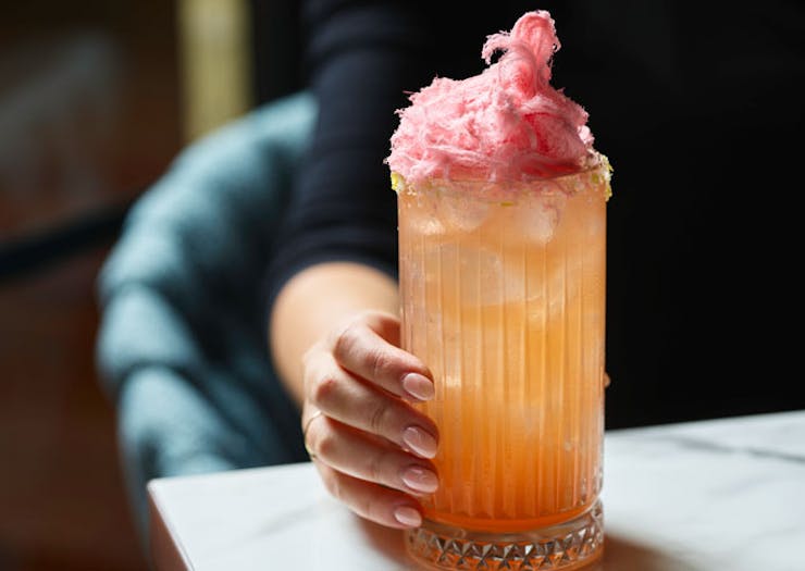 A large peach-coloured cocktail topped with fairy floss
