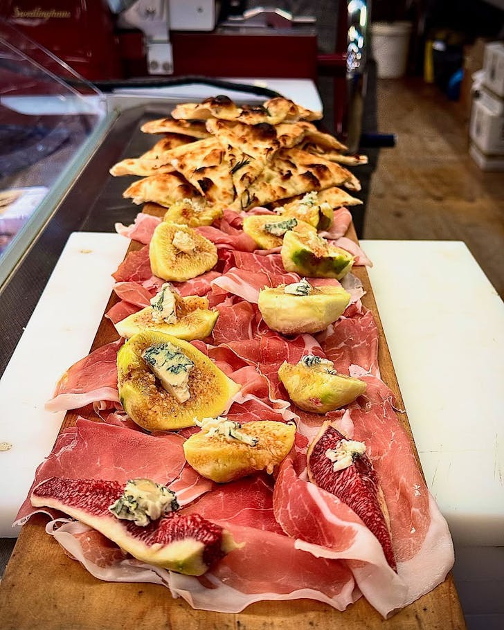 A long wooden board topped with pancetta, figs and hunks of blue cheese. 