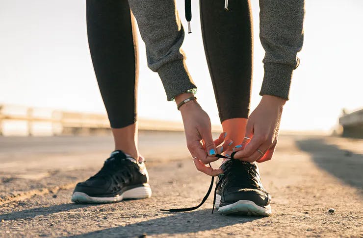 A woman bends to tie up her shoe laces before going for a run.
