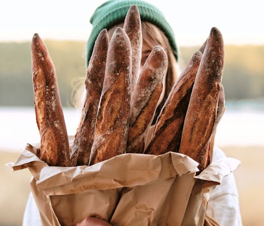 A person holding a bag of baguettes from Lagom Bakery