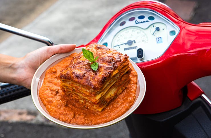 a plate of saucy lasagne in front of red scooter