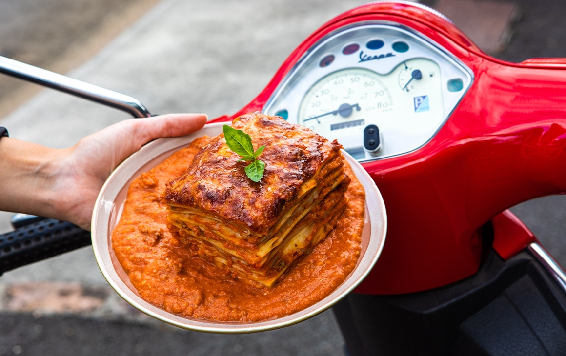 a plate of saucy lasagne in front of red scooter