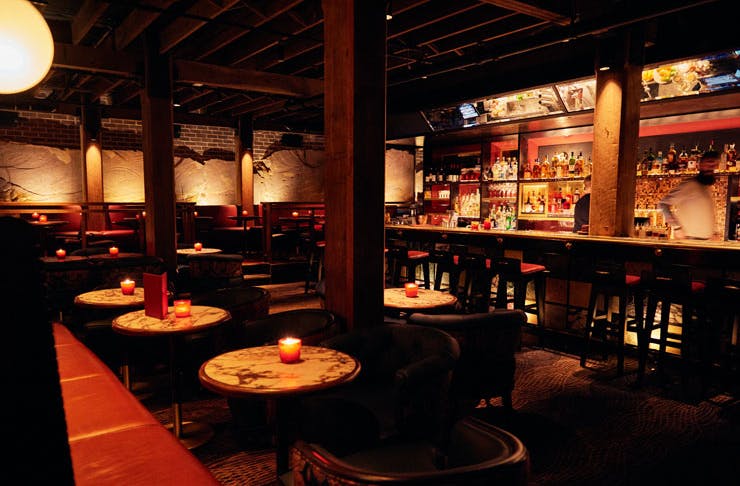 A dimly lit bar with red leather couches and candles. 