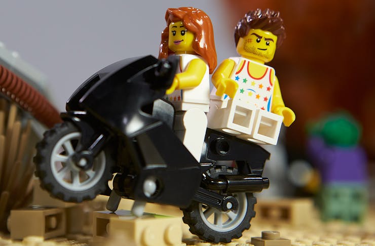 A male and female LEGO figure sit on the back of a bike.