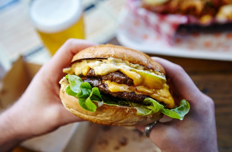 Two hands holding a big juicy cheeseburger.
