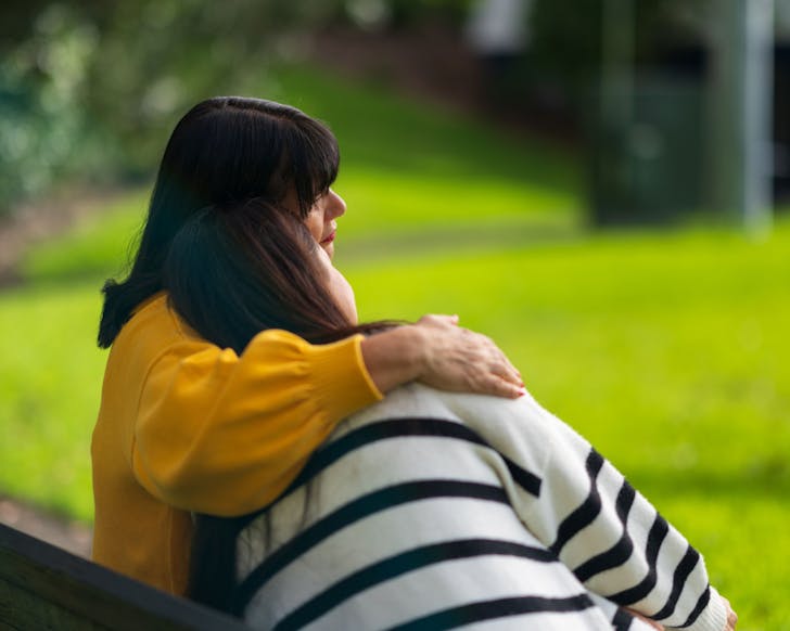 One person comforts another on a park bench.