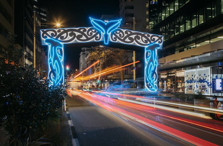 A neon-lit Te Wehenga Moana archway—traditional Māori designs and a whale's tale in the middle arch—above a road in the city centre.