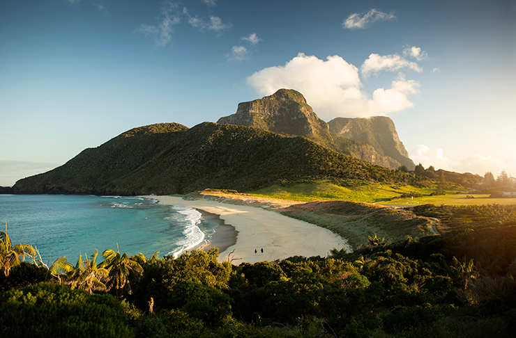 The coastline of Lorde Howe Island surrounded by mountains on a sunny afternoon.