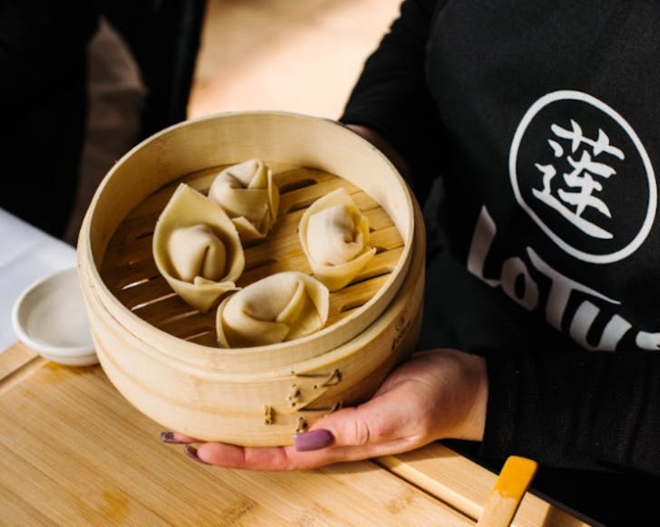 A close up image of two hands holding a steam tray of dumplings. 