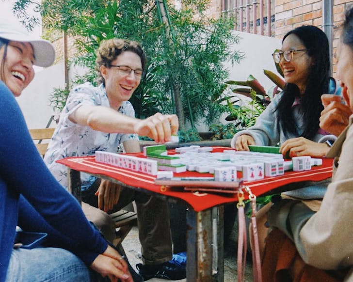 Young people laughing play Mahjong at a table outside.