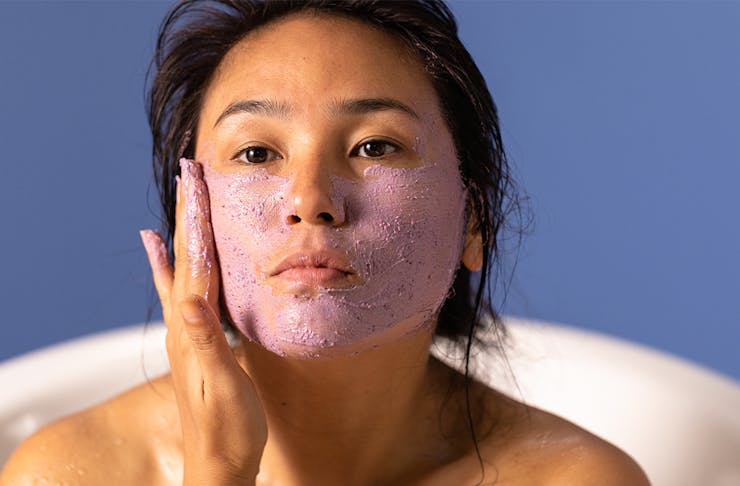 a woman rubbing a purple clay mask on her face