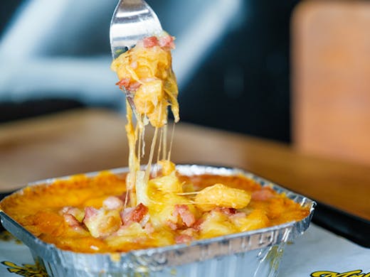 A Fork digging into an alfoil container of mac and cheese