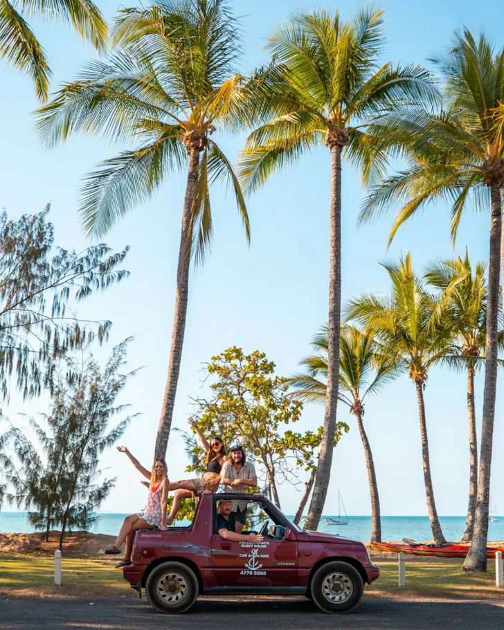 A group of friends sitting in a topless car against swaying palm trees on Magnetic Island.