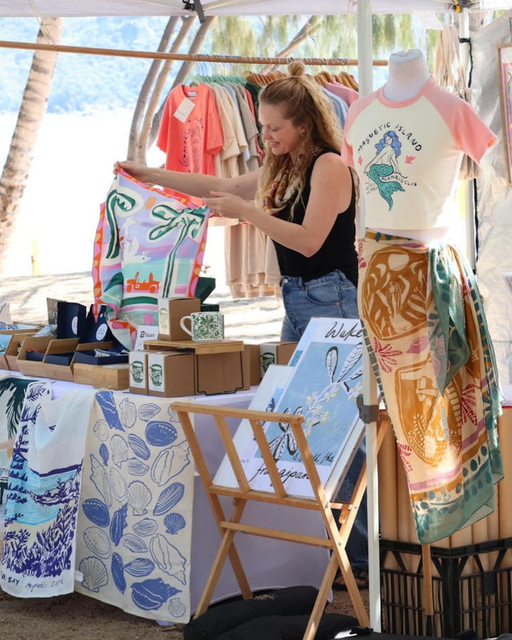 A market stallholder holds up an artwork against the backdrop of the Coral Sea on Magnetic Island.