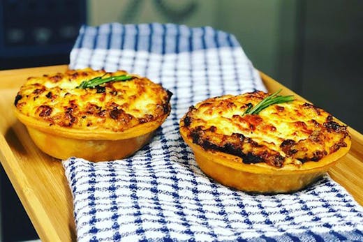 Two just-baked moussaka pies just out of the oven, placed on a wooden board.
