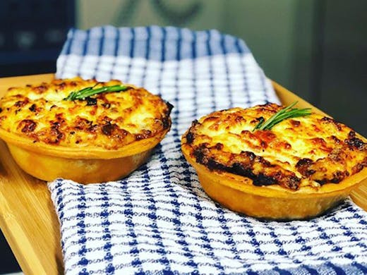 Two just-baked moussaka pies just out of the oven, placed on a wooden board.