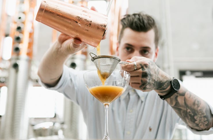 A bar tender at Fortune Distillery in Noosa, pours a cocktail into a glass from a copper-coloured shaker. 