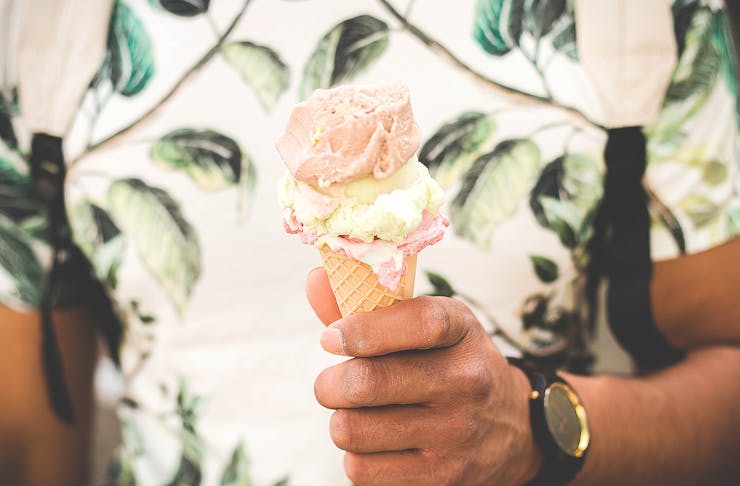 A man holds an ice cream in his hands wearing a summery shirt.