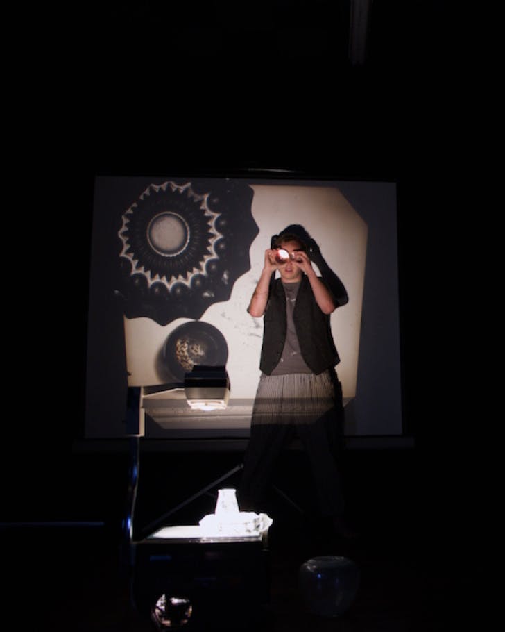Adam Rohe performs his Marble Universe one-man show with an overhead projecting screening into him and onto a white screen behind him.
