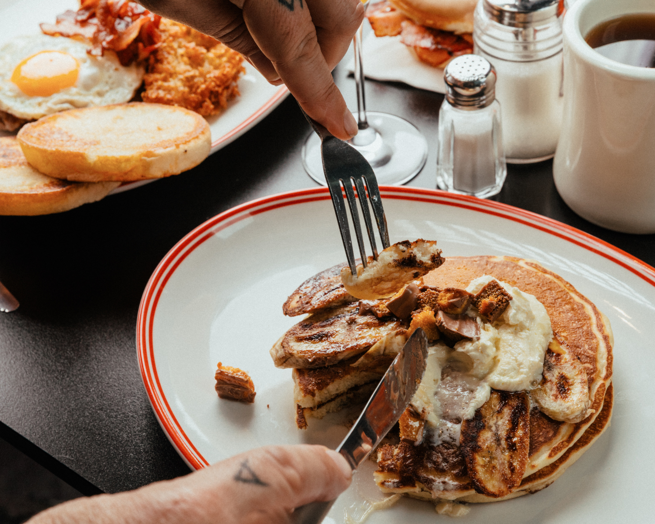 mary's bottomless and brunch menu person cuts into a stack of pancakes with butter and bacon alongside a full table of breakfast treats