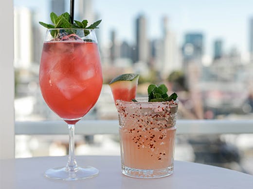 Two cocktails in front of a distant city skyline. 