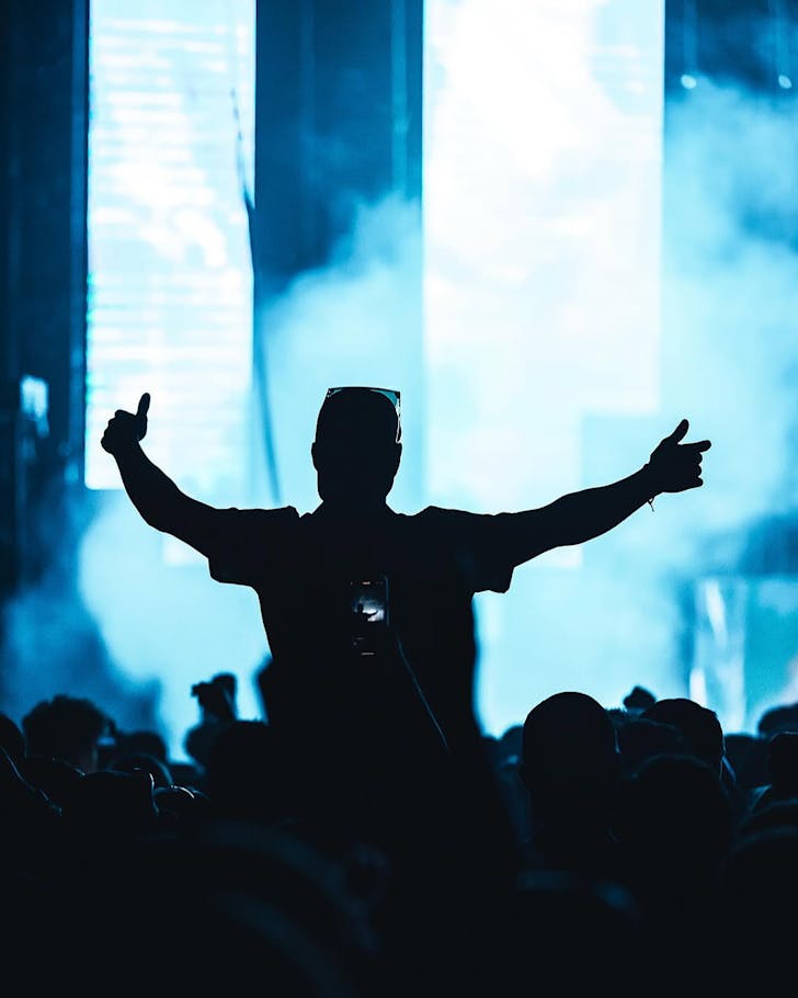 Someone sits on another's shoulders amongst a blue-lit crowd at Mayhem Festival.