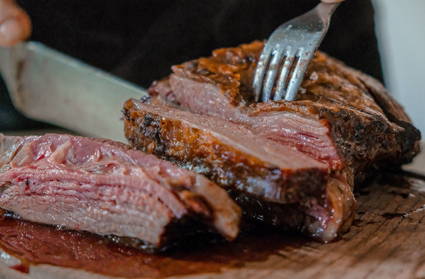 A hand cutting a piece of smoked BBQ meat with fork and knife