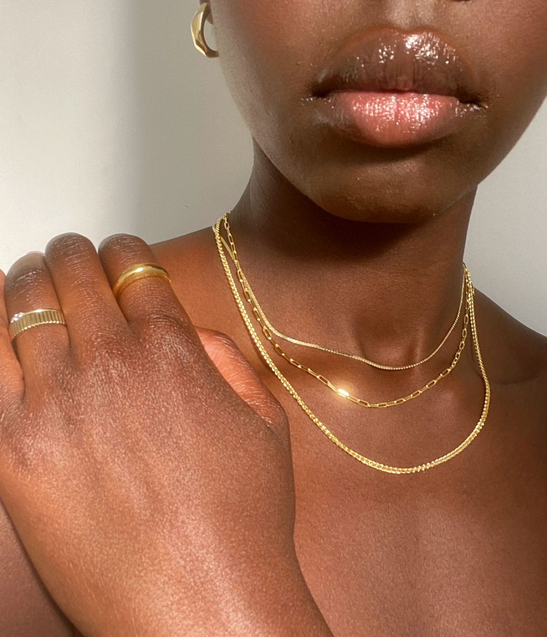a woman wearing gold chains and rings, only her hand and shoulders are visible
