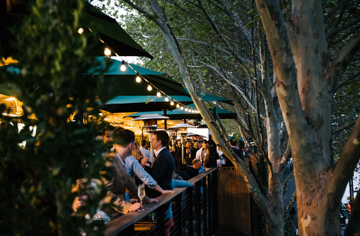 A long beer garden in Melbourne where people after work are drinking beers in the sun.