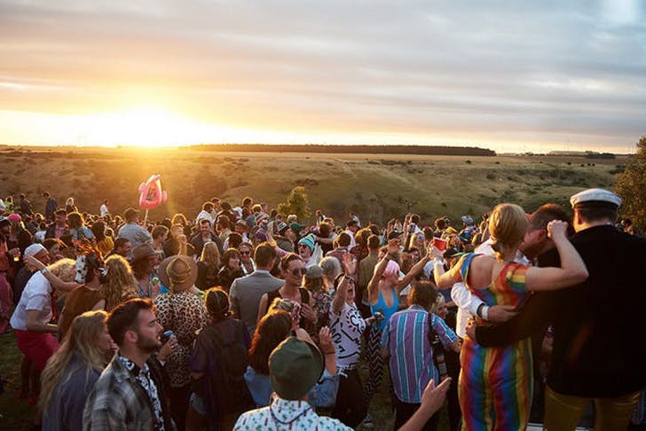Festival-goers at Meredith overlooking the sunset across several grassy paddocks.