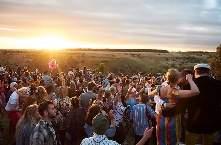 Festival-goers at Meredith overlooking the sunset across several grassy paddocks.