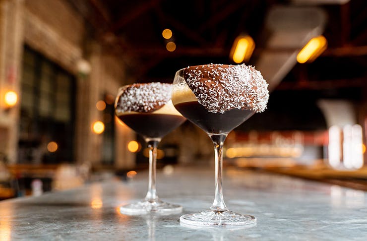 Two espresso martinis on a marble table. Chocolate is dripping from the rim of the glass.