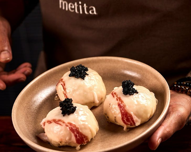 A chef holds a plate of three corned beef steamed buns topped with fish roe.