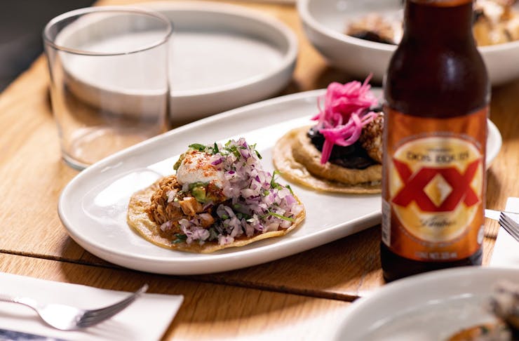 two tacos on a plate with a mexican beer bottle