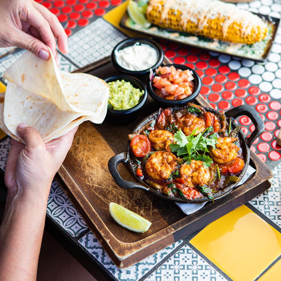 a person pulling soft tortillas apart over a sizzling plate of prawns