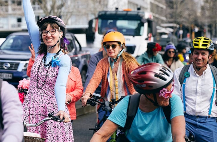 People in colourful clothes cycle together through the city.