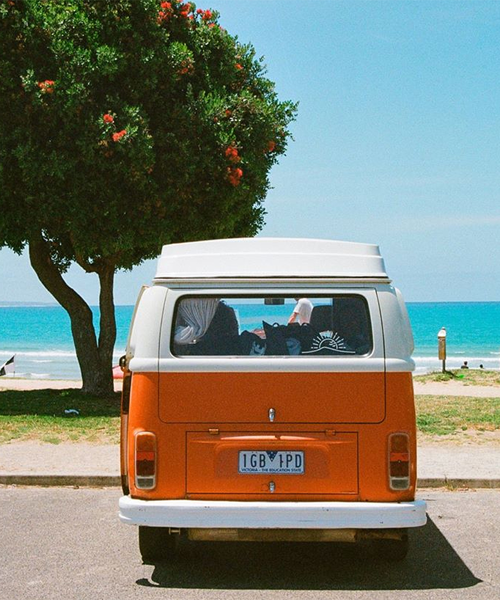 A cute little Mighway orange combi sits on the seaside.