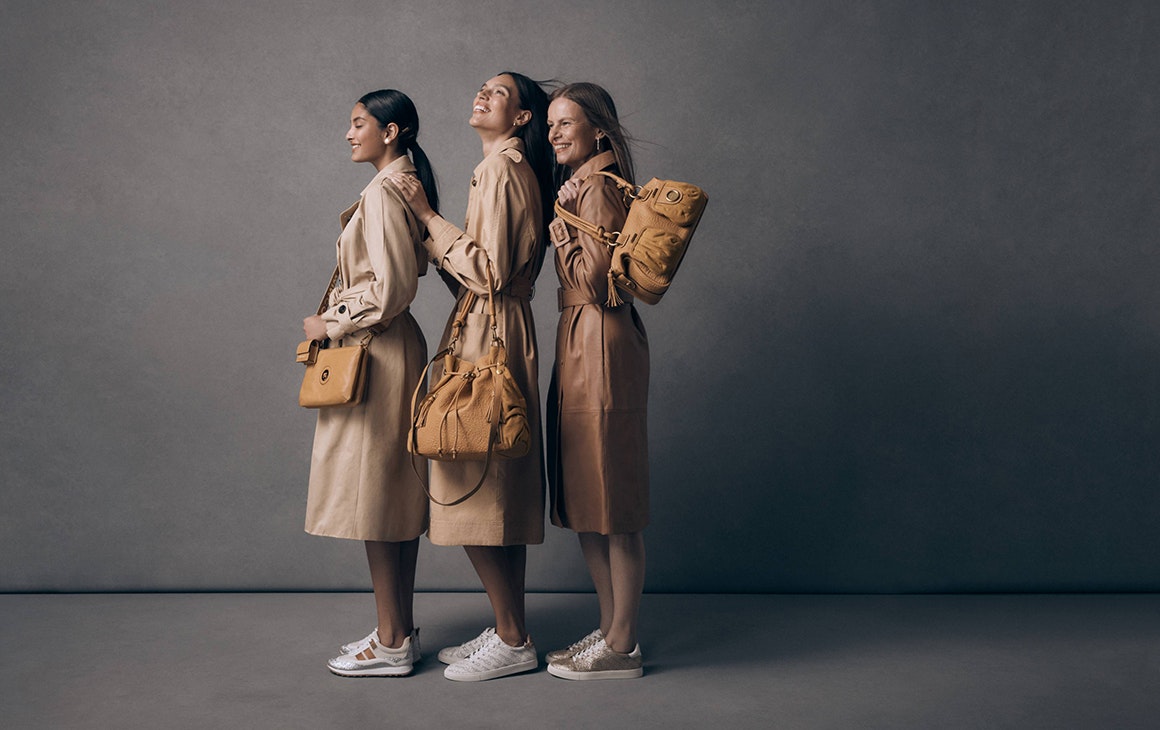 three women in trench coats holding tan handbags