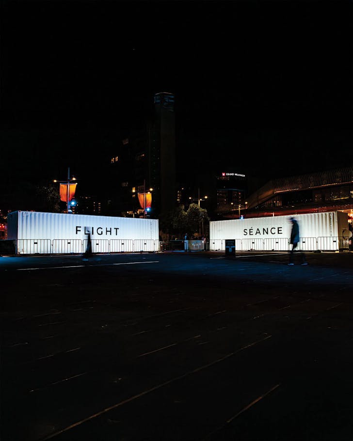 The white shipping containers of SÃANCE and FLIGHT illuminated at night.