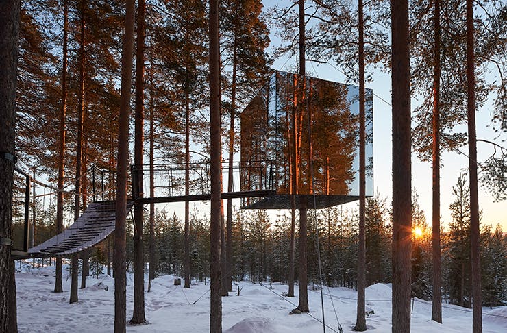 A mirrored cube perched on a tree in snowy Swedish mountains.