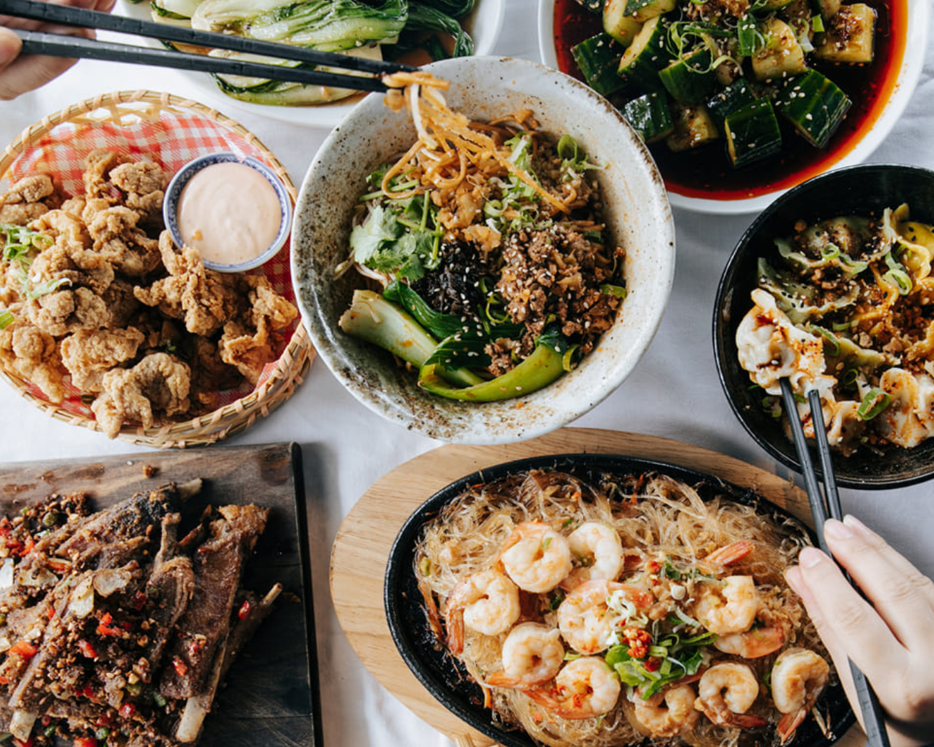 Two chopstick-wielding hands dig in to a delicious spread of spicy Sichuan dishes at Miss Peppercorn 