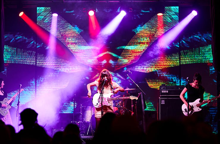 A woman on a neon-lit stage holding a guitar.
