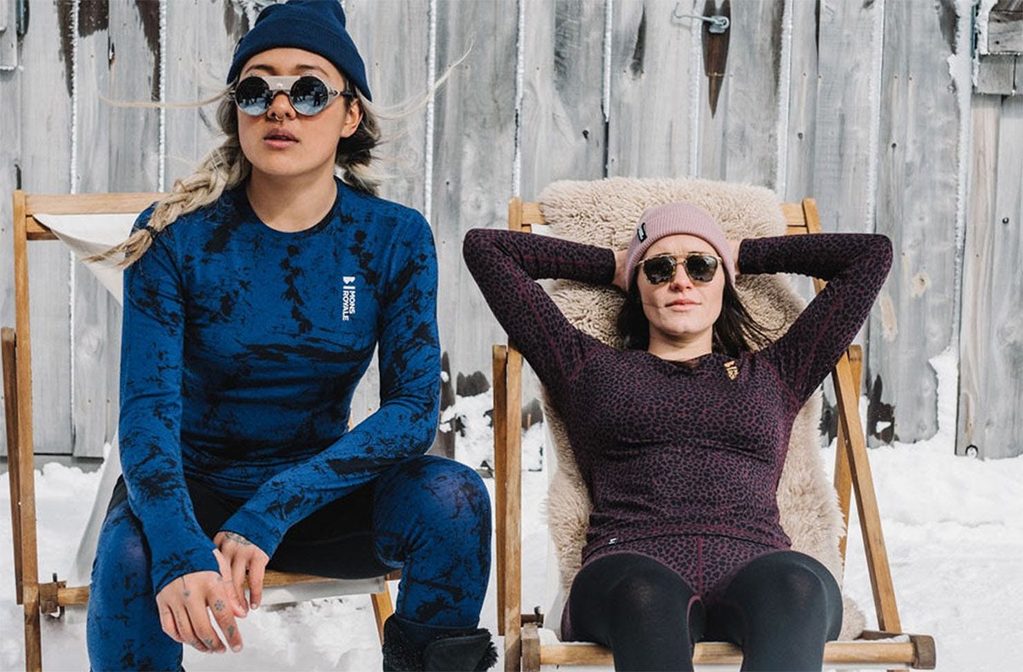 Two people clad in Mons Royale merino baselayers, beanies and sunglasses kick back on chairs in the snow. 