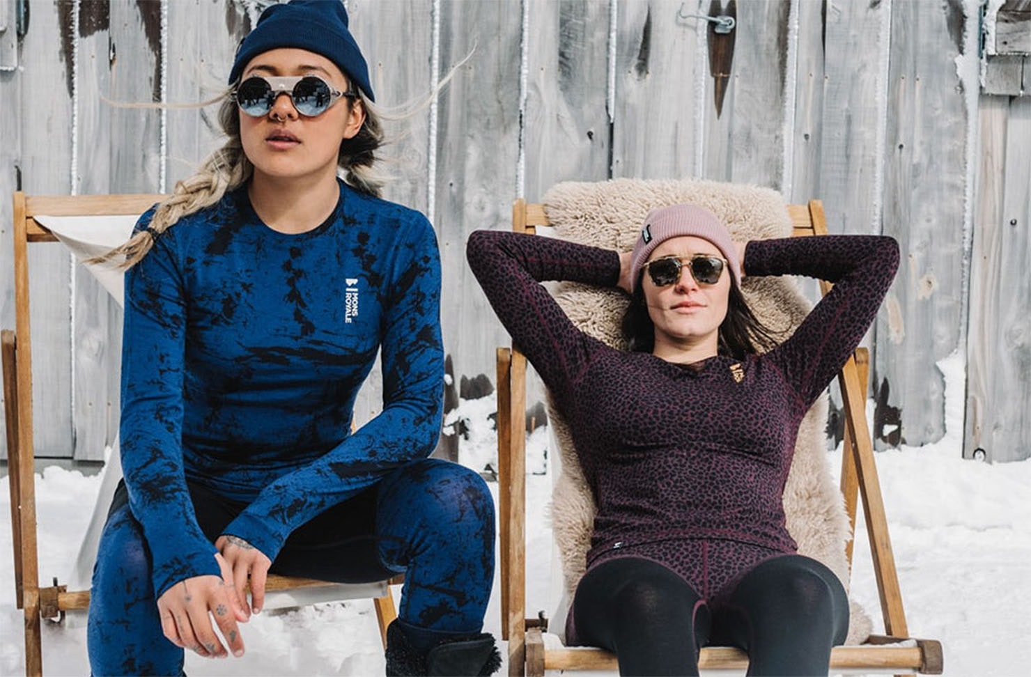 Two people clad in Mons Royale merino baselayers, beanies and sunglasses kick back on chairs in the snow. 